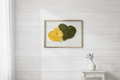 Pressed Yellow flower and green leaves in shape of 2 hearts on a white background with a gold frame.
