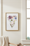 Heart-shaped arrangement of pressed flowers with a gold frame on a white background