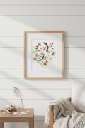 Heart-shaped arrangement of flowers and leaves in a gold frame on a white background