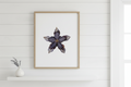 Framed artwork of a pressed flower with a gold frame on a white background