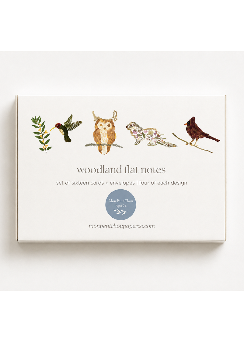 A boxed set of woodland flat notes cards and envelopes on a clean white background. The front of the box shows illustrated nature motifs: a hummingbird, owl, fox, and bird, with the text 'woodland flat notes' and 'set of sixteen cards + envelopes | four of each design.