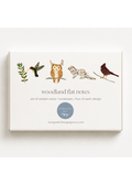 A boxed set of woodland flat notes cards and envelopes on a clean white background. The front of the box shows illustrated nature motifs: a hummingbird, owl, fox, and bird, with the text 'woodland flat notes' and 'set of sixteen cards + envelopes | four of each design.