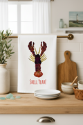 Kitchen towel with a colorful lobster design and 'Shell Yeah!' text, placed on a kitchen counter.